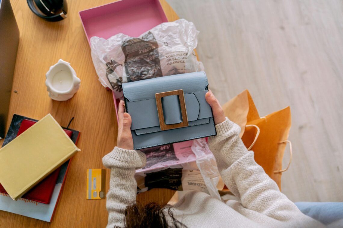 A person unboxes a chic blue handbag at home, surrounded by paper and shopping bags.